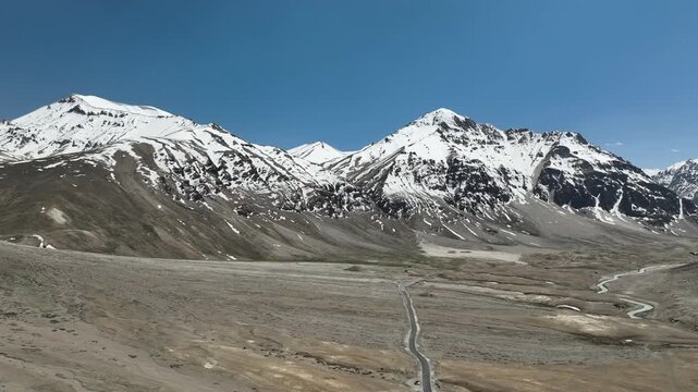 Aerial view of huge snow-covered Himalayan mountain range rising above brown rocky slopes and a deep valley in Zanskar Ladakh India shot by a drone

