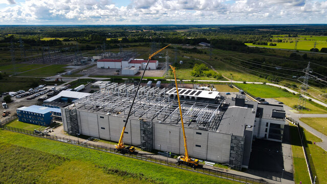 Large data center facility under construction with cranes and heavy equipment, integrating with a powerful electrical substation and extensive infrastructure