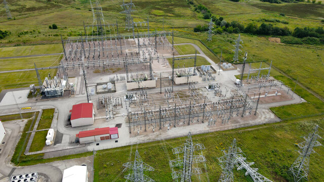 Aerial view shows a large scale electrical substation with extensive high voltage power lines. Transformers. And switchyards