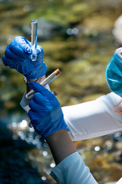 industrial wastewater testing river landscape with copy space for banner design, person in blue gloves holding glass tube with water sample, testing for heavy metal poisoning and chemical pollution