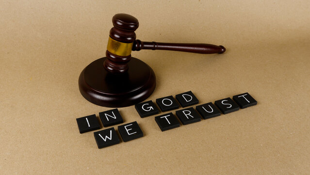 Gavel resting near letter tiles spelling In God We Trust, symbolizing the foundational principles of law, justice, and societal trust within a judicial context