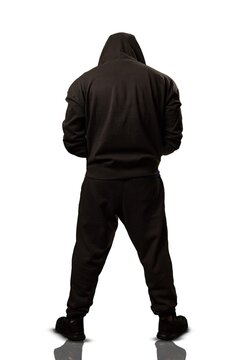 Full length studio shot of a man from the back wearing a dark black hoodie and matching sweatpants standing against a solid white background with shadows.