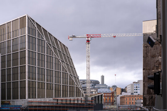 Modern architecture and construction in Oslo frame an office building beside a tower crane with geometric facade lines beneath an overcast urban sky