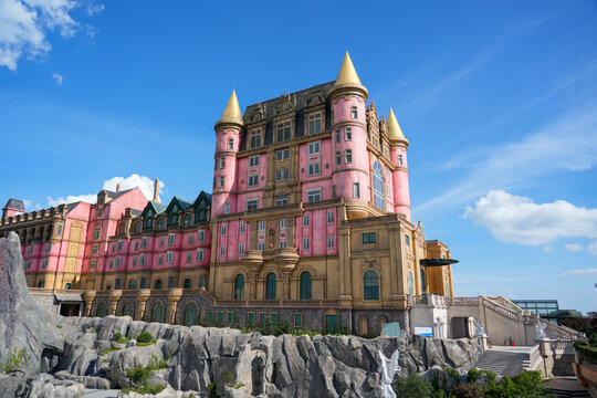 Visitors marvel at the grand castle with its pink walls and golden spires, set against a stunning blue sky and rocky terrain, creating a magical atmosphere. Vietnam, Bana hills, Danang
