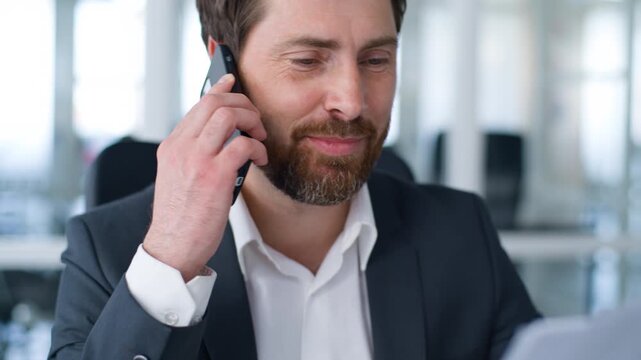 Smiling joyful Caucasian middle-aged business man communicating smartphone call with papers mature businessman smile positive talking mobile phone conversation with documents male executive at office