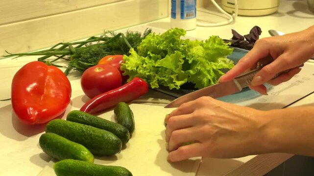 Person slicing fresh organic vegetables in a bright kitchen to prepare a healthy green salad, culinary lifestyle, fresh food preparation, healthy eating concept, home cooking.
