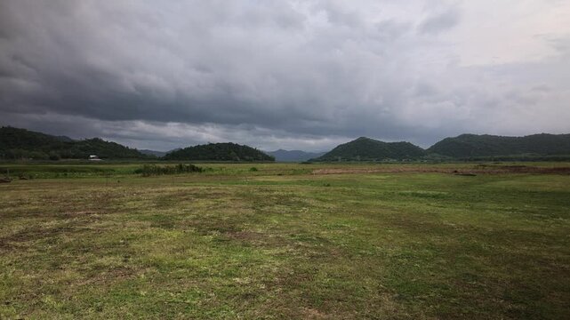 Static wide shot of an empty grassland plain stretching to distant green mountains under heavy grey monsoon rain clouds