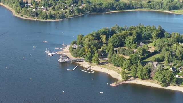 Lac des Settons in Morvan, France, showing a scenic lakeshore with a sandy beach, marina, docks, and lush green trees, aerial view.