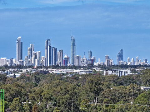 Aerial view of the Surfers Paradise skyline featuring modern skyscrapers rising above lush green vegetation under a clear blue sky in Surfers Paradise, Queensland, Australia.