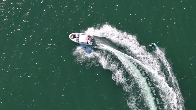 Aerial view of a motorboat towing a person on a water tube across the calm sea in Cascais, Lisbon, Portugal.