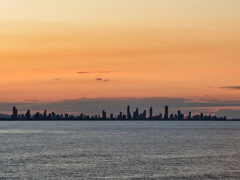 Aerial view of the Surfers Paradise skyline silhouetted against a vibrant sunset sky over the ocean in Surfers Paradise, Queensland, Australia.