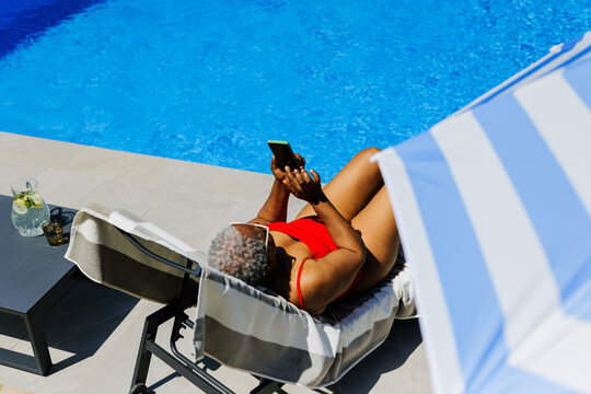 Woman relaxing by swimming pool using smartphone
