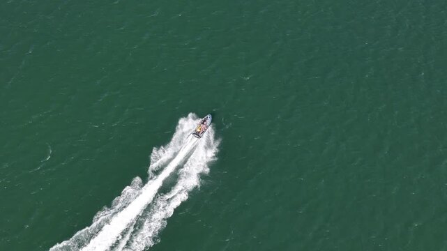 Aerial view of a jetski speeding across the green water leaving a white wake in Cascais, Lisbon, Portugal.