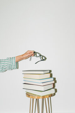 Hand Holding Eyeglasses Above Stack of Books
