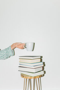 Hand Holding Coffee Mug Above Stack of Books