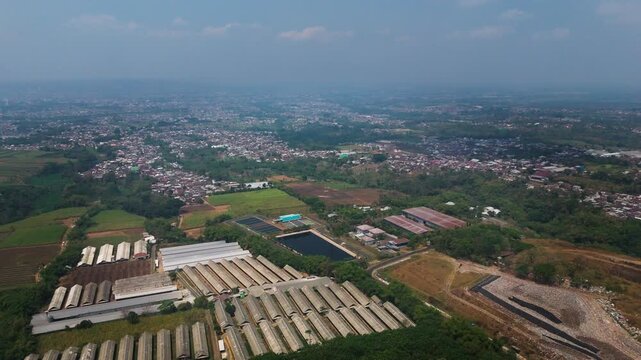 Aerial view of the leachate treatment plant and retention ponds at TPA Supit Urang surrounded by lush vegetation and urban landscape in Malang, East Java, Indonesia.