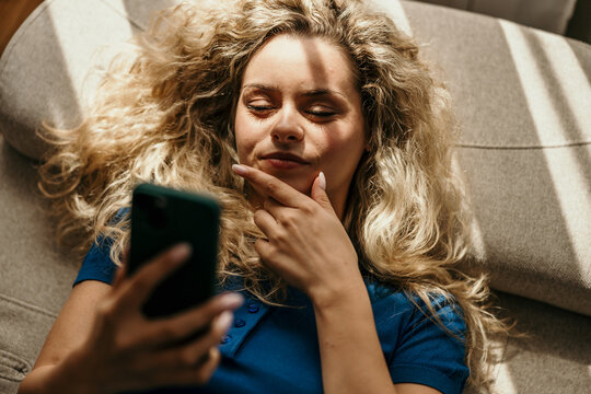 Young woman relaxing on sofa contemplating smartphone content