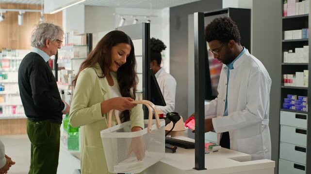 Indian young woman and old Caucasian man clients buying pills in pharmacy talking with African American pharmacists sellers working in drugstore different ages multiethnic customers buy medicine aid