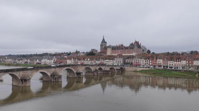 The city center of Gien, France, featuring the iconic stone bridge crossing the Loire River, traditional French townhouses, and the prominent chateau on the hill, wide shot.