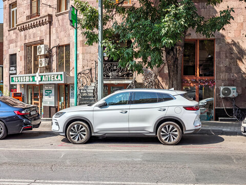 Modern white SUV parked on city street with trees and buildings nearby