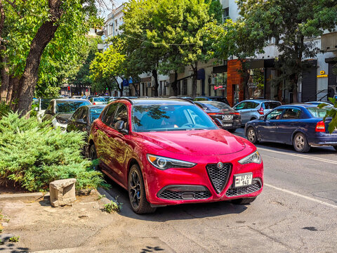 Red car parked on tree-lined city street with other vehicles
