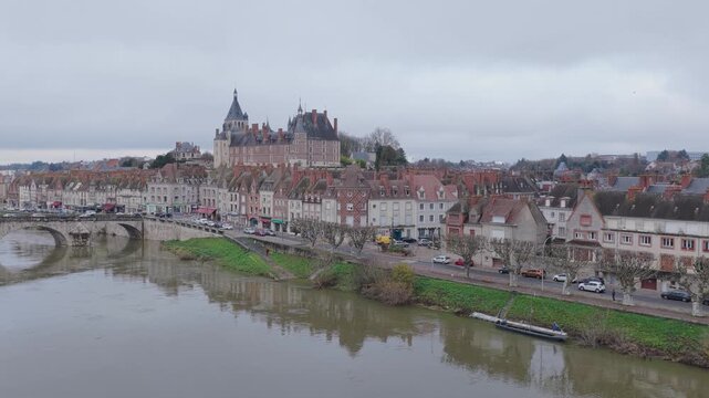The historic cityscape of Gien, France, showcasing the town center with traditional French architecture, the prominent chateau, and the Loire River in the foreground, aerial view.