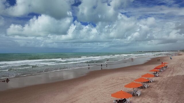 Aerial view of the sandy beach with orange umbrellas and people walking along the shoreline in Maragogi, Alagoas, Brazil.