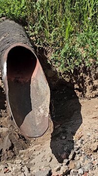 Water flows through a large pipe near a construction site in the afternoon sun