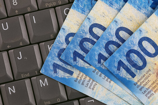 Swiss banknotes, each with a face value of 100 francs, and a computer keyboard