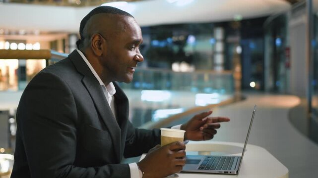 African American mature business man with coffee talking video call laptop chat smiling laughing middle-aged businessman male executive employer talk with computer conference smile enjoy negotiation