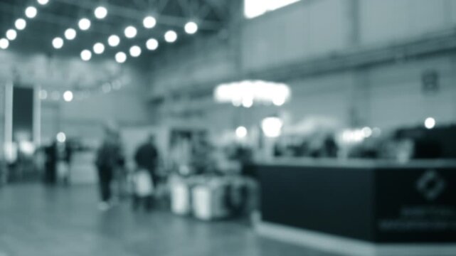 Blurred background. Many people walking inside large building. Men and women walking on floor inside room with high ceiling and large lanterns on walls. Public place. Exhibition presentation backdrop