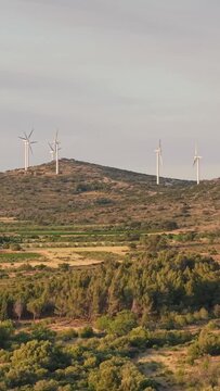Several wind turbines on a hilltop surrounded by Mediterranean vegetation and rolling countryside in Opoul Perillos, southern France, vertical 9:16 view.