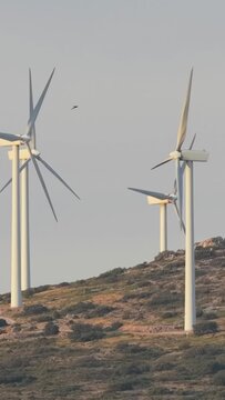 Several large wind turbines rotating on a grassy, rocky hillside in Opoul Perillos, southern France, vertical 9:16 view.