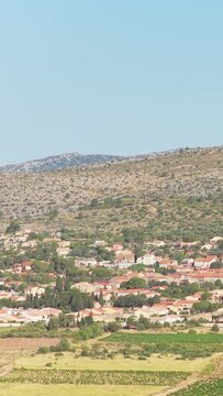 The village of Opoul Perillos in southern France, framed by rolling hills and agricultural fields under a clear blue sky, aerial vertical 9:16 view.