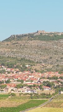 The village of Opoul Perillos in southern France, with its distinctive red-roofed houses surrounded by vineyards and fields, aerial vertical 9:16 view.