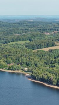 The lush green forests and calm shoreline of Lac des Settons in Morvan, France, aerial vertical 9:16 view.