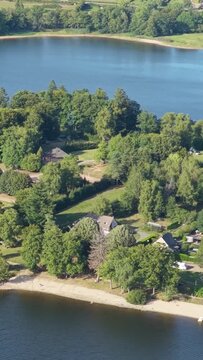A lush green lakeshore with houses nestled among trees at Lac des Settons in Morvan, France, aerial vertical 9:16 view.
