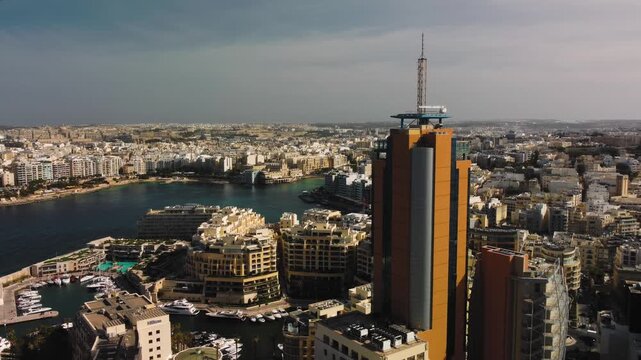 serene seaside cityscape with tall buildings and calm sea in aerial perspective featuring concrete and glass materials under blue sky and brown earth tones, urban skyline static view.