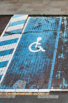 Accessible parking space featuring a white wheelchair symbol painted on blue pavement next to a pedestrian ramp and curb in Firgas.