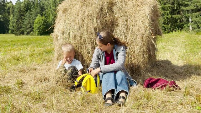 A mother and young son sit and rest by a large haystack in a sunny park. They feel happy, peaceful, and relaxed during this joyful outdoor break.