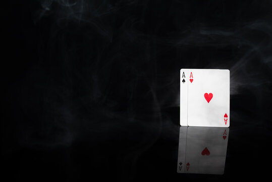 Ace of hearts and ace of spades playing cards in dramatic smoke on black background with reflection. Concept of luck, risk, gambling, strategy and winning hand.
