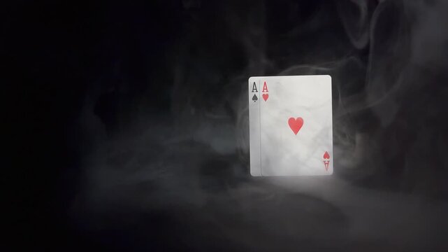 Slow motion ace of hearts and ace of spades playing cards in dramatic swirling smoke on black background with reflection. Concept of luck, risk and gambling.