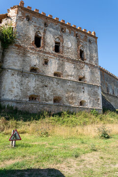 Ruined stone palace facade of Medzhybizh fortress behind warning road sign