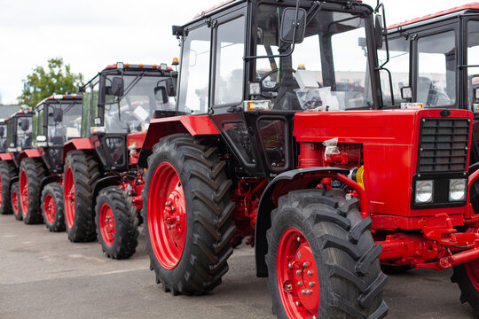 Row of new red tractors parked at dealership or manufacturing facility. Modern agriculture, industrial power, machinery supply.
