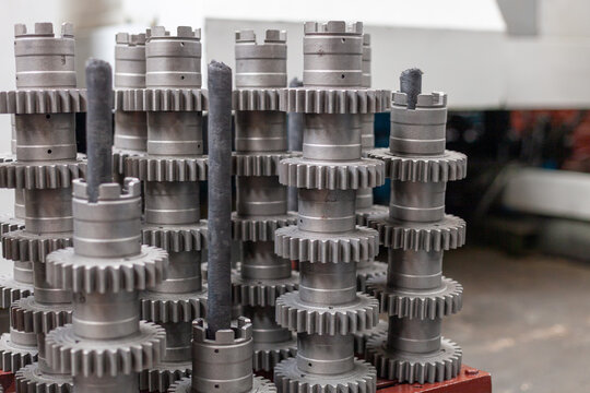 Close-up view of several freshly machined metal gear shafts on production line at heavy machinery manufacturing plant. Mechanical engineering, precision parts production,  modern factory automation.