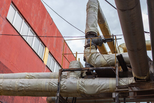 Industrial exterior with insulated pipes and red building wall. Industrial infrastructure, energy supply, engineering, maintenance, factory exterior, urban development, heating system, heavy industry.