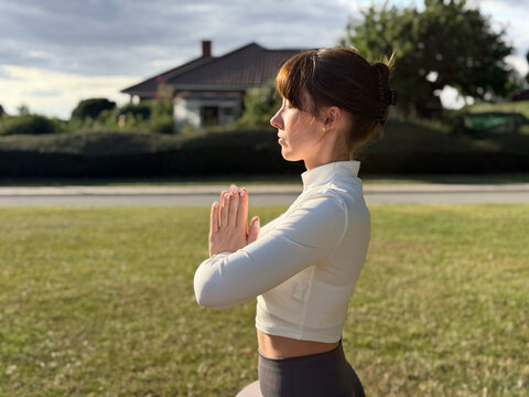 A woman practicing yoga outdoors with hands in prayer position.