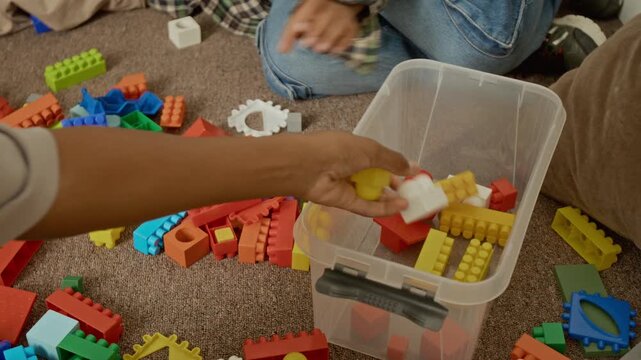 Children cleaning up colorful toy blocks into plastic container while sitting on floor. Video suitable for early education marketing, parenting blogs, and toy commercials