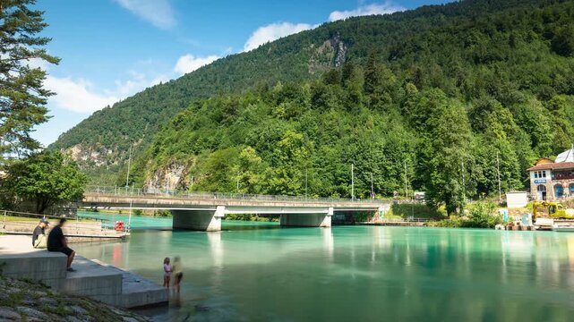Turquoise Aare river time lapse in Interlaken with Harderbahn funicular railway ascending mountain, green forest, and concrete bridge in Switzerland