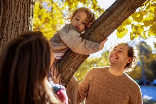 Father smiling at son climbing tree in autumn park